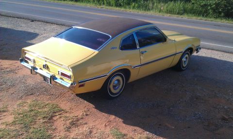 1965 Ford Mustang - This yellow coupe is parked on the side of a road, showing its rear and side profile.
