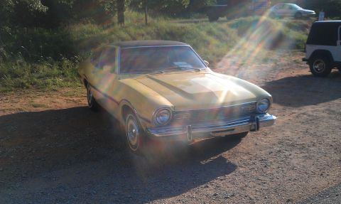 1965 Ford Mustang - A yellow 1970 Ford Maverick is parked outdoors with other vehicles visible in the background.