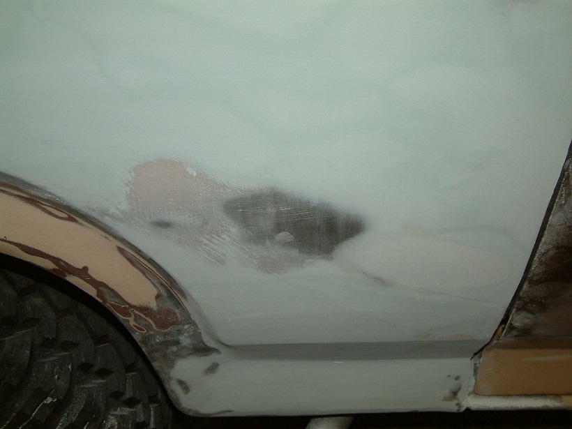 Close-up of car bodywork with primer and filler, showing repair work on the rear fender area