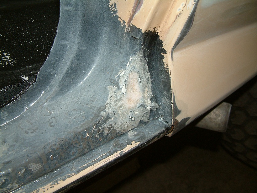 Close-up of rust damage on a vehicle's door frame, showing exposed metal and primer
