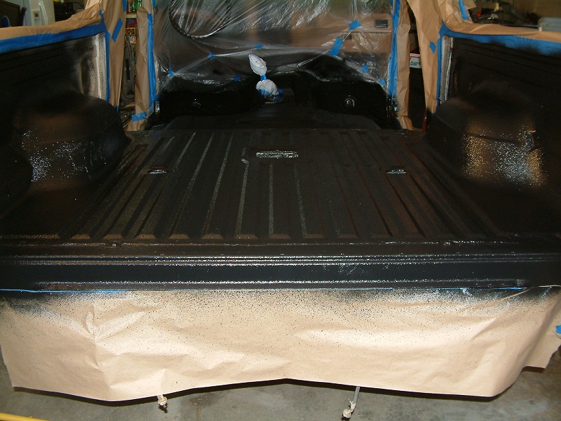 truck bed with black spray paint applied, masking paper on the tailgate