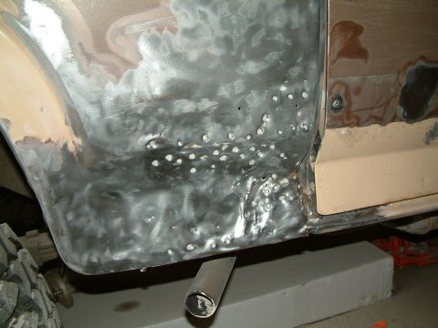 1983 Ford Bronco - Close-up of a vehicle's lower body panel undergoing repair, revealing areas of rust and welding.