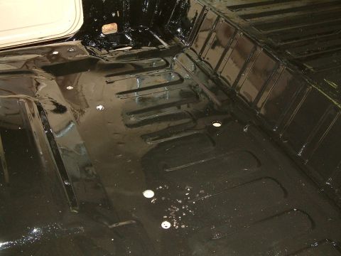 1983 Ford Bronco - Interior floor pan of a 1983 Ford Bronco, coated in black with visible mounting points.