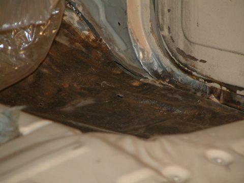 1983 Ford Bronco - Close-up view of significant rust damage on the floor pan and rocker panel of a vehicle.