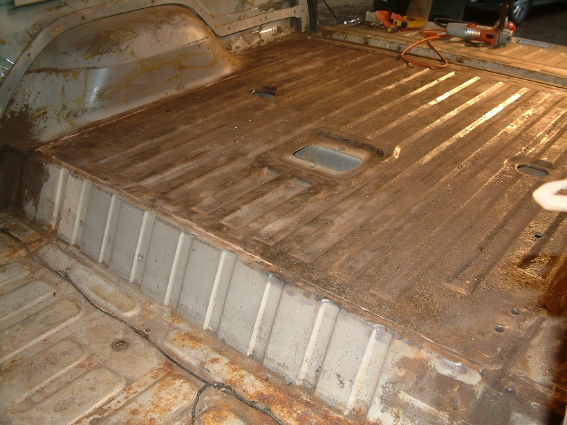 Interior of a vehicle with floor stripped down to metal, showing rust and some repair work