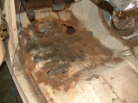 1983 Ford Bronco - The interior floor pan of a vehicle shows extensive rust damage and holes, with pedals visible.