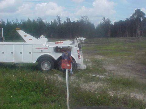 1996 Ford Bronco - A tow truck is parked in an open field with trees in the background.