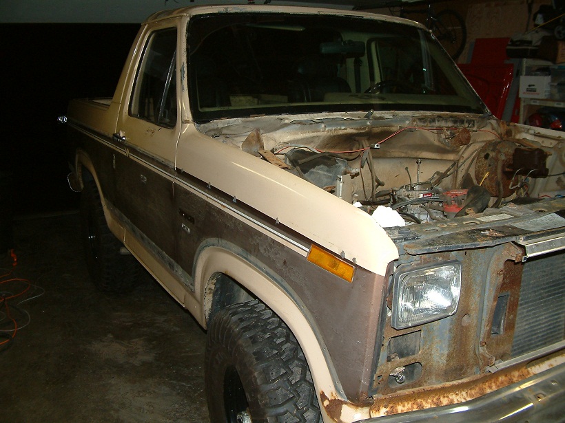 Brown and tan Ford Bronco with hood open, showing engine bay. Rust visible on front fender