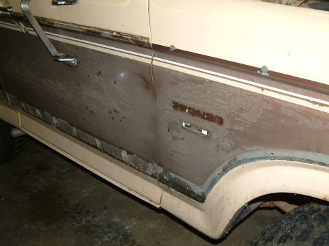 1983 Ford Bronco - Close-up of the side of a 1983 Ford Bronco, showing its distinctive woodgrain trim and weathered appearance.