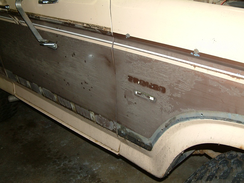 Side view of a 1983 Ford Bronco with woodgrain paneling and chrome trim. The paint is faded and there are some dents