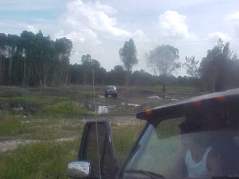 1996 Ford Bronco - A 1996 Ford Bronco navigates a muddy, off-road terrain with trees in the background and another vehicle visible.