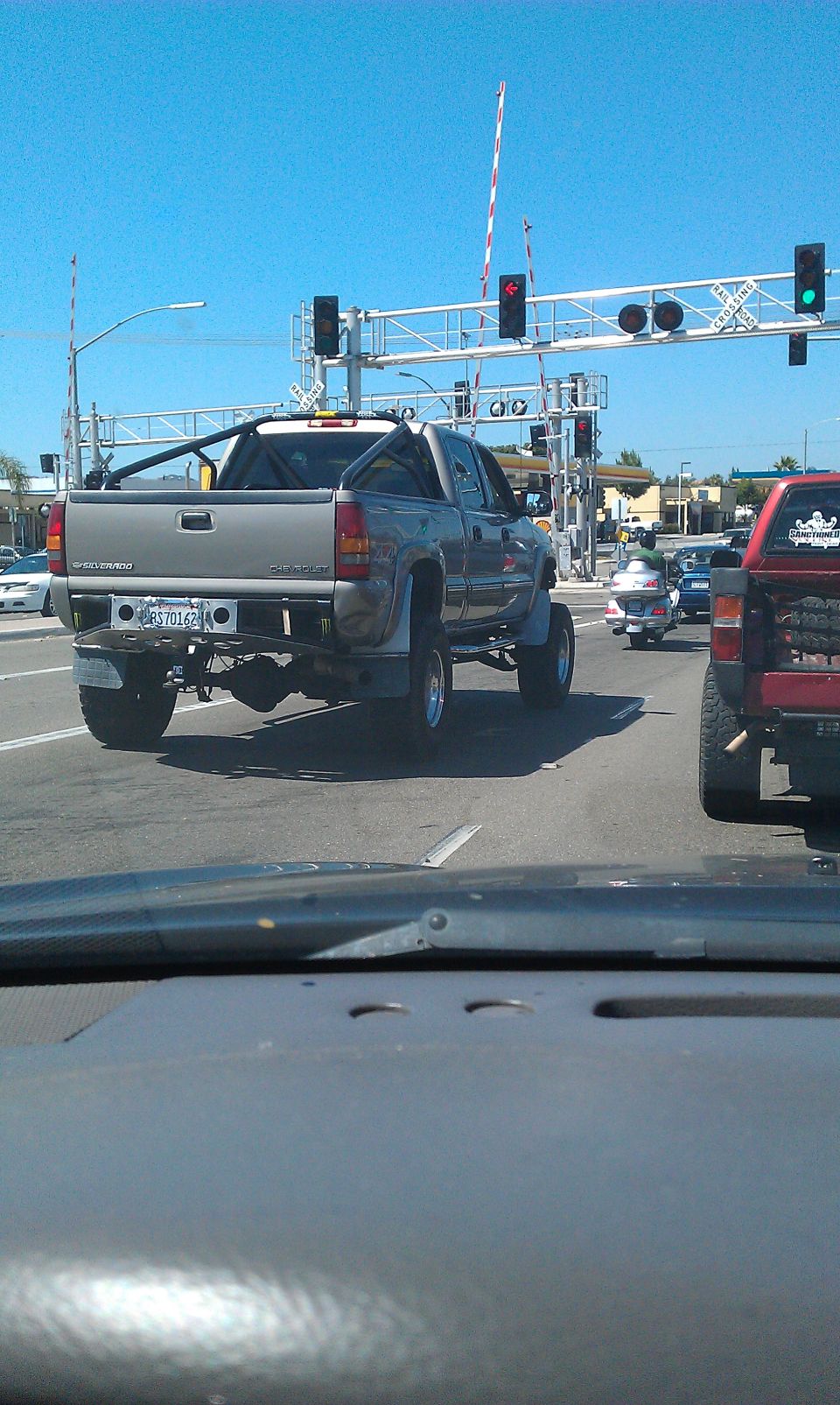 Silver pickup truck with a roll bar, lifted suspension, and aftermarket bumper at a railroad crossing