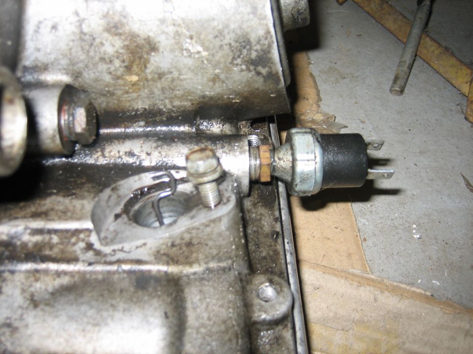 Close-up of an oil pressure sensor screwed into an engine block. A bolt is also visible in the block