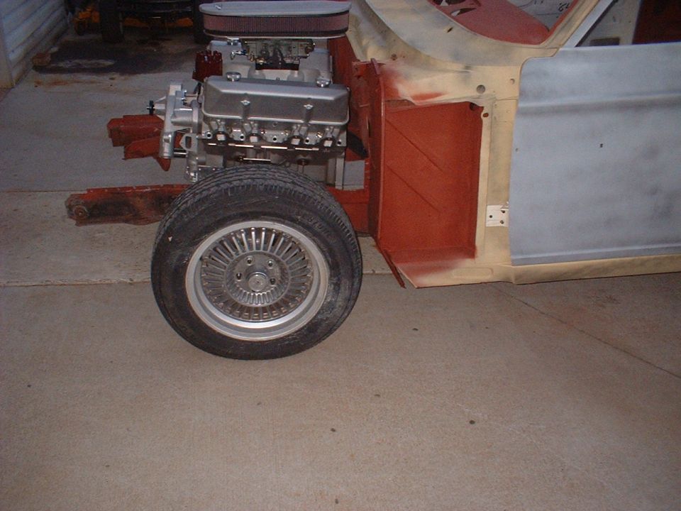 Car chassis with engine and front wheel installed, undergoing restoration