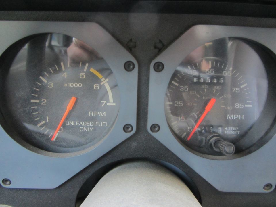 1985 Ford Mustang dashboard with tachometer and speedometer gauges. Tachometer reads RPM and "UNLEADED FUEL ONLY". Speedometer reads MPH and KM/H