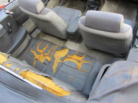 1985 Ford Mustang - The interior of this convertible shows significant wear and tear on the seats, with the upholstery ripped and exposing the underlying foam.