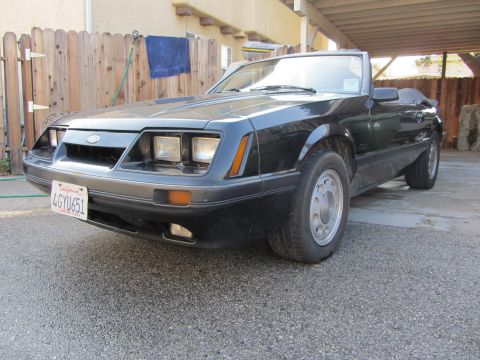 1985 Ford Mustang - This black 1985 Ford Mustang convertible is shown from the front 3/4 angle, parked outdoors.