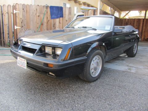 1985 Ford Mustang - This black 1985 Ford Mustang convertible is parked in a driveway.