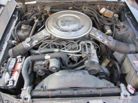 1985 Ford Mustang - Overhead engine-bay shot of a dusty carbureted Ford 5.0 V8, with the round air cleaner lid stamped '5.0 Liter 4V H.O.' over a four-barrel c…