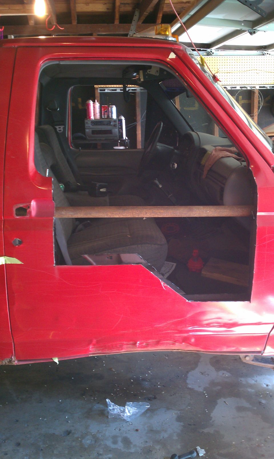 Red truck cab interior with cut-out door, showing seats and dashboard. A wooden bar is across the opening