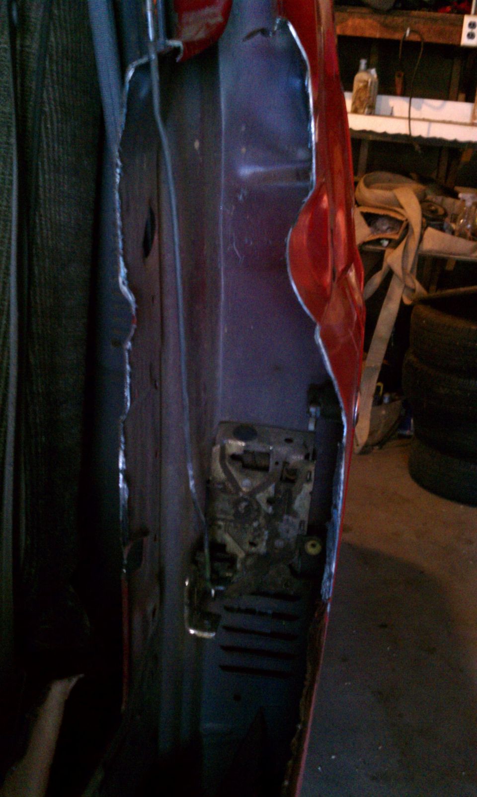 Red vehicle door interior with exposed latch mechanism and torn metal
