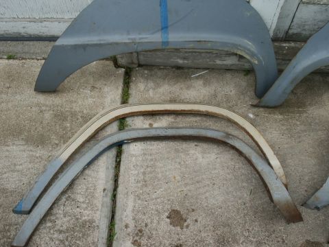 1966 Ford Bronco - Various car fender parts and trim pieces are shown on a concrete surface.