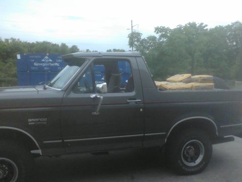 1988 Ford Bronco - A dark gray Ford Bronco is seen from the side, loaded with bags of cement in its cargo area.