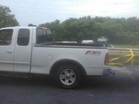 1988 Ford Bronco - White pickup truck bed loaded with lumber, FX4 Off Road decal visible.