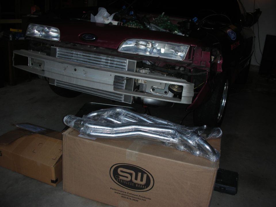 car front end with bumper removed, new exhaust headers on a box in front