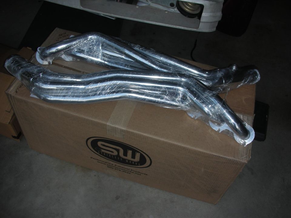 Exhaust headers wrapped in plastic on a cardboard box with SW logo