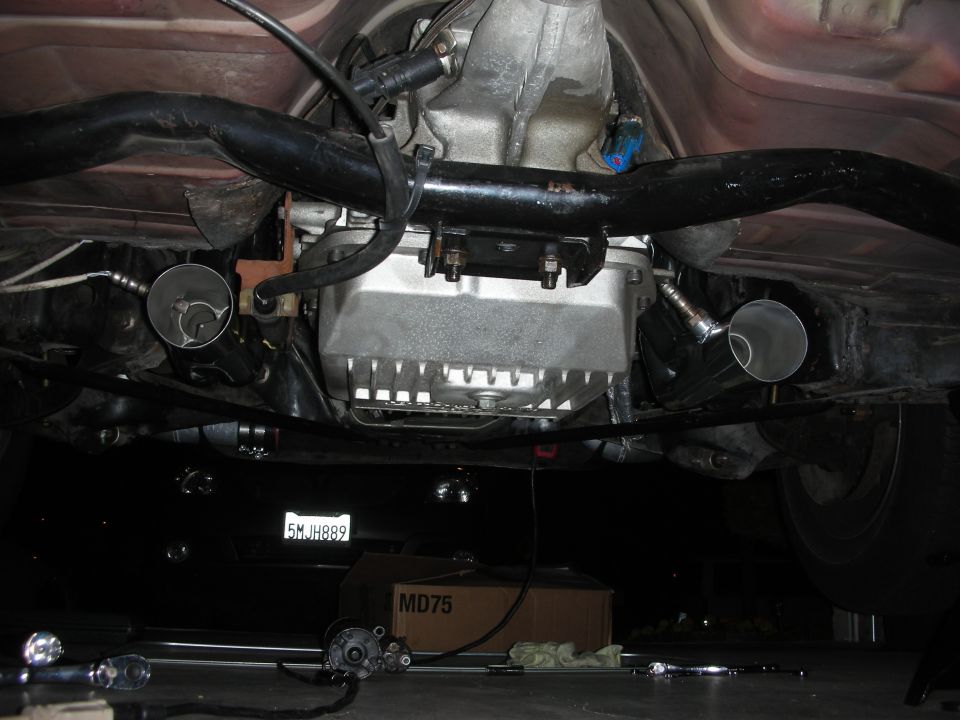 Underside of a vehicle showing transmission pan, exhaust pipes, and a license plate reading 5MJH889