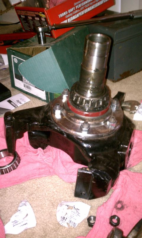 1990 Ford Bronco - A vehicle spindle assembly with bearings is shown, surrounded by tools and parts on a carpeted floor.