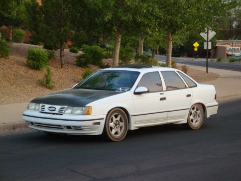 1990 Ford Taurus - White 1990 Ford Taurus sedan with a black hood parked curbside.
