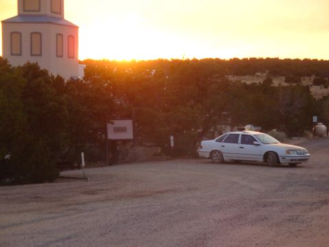1990 Ford Taurus - A white 1990 Ford Taurus sedan is parked near a building during a New Mexico sunset.