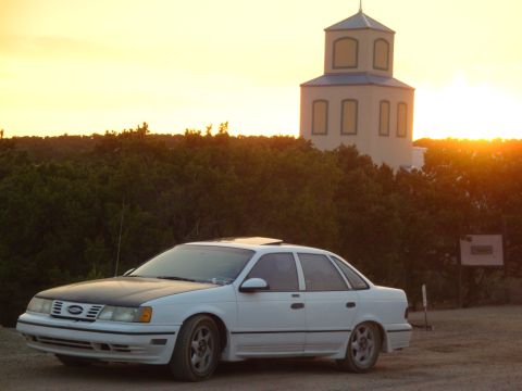 1990 Ford Taurus - White 1990 Ford Taurus sedan parked in front of a building at sunset.