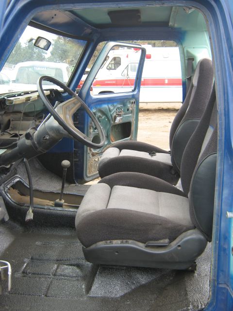 1978 Ford Bronco - Interior view of a blue truck with bucket seats, steering wheel, and gear shifter. An ambulance is visible outside.