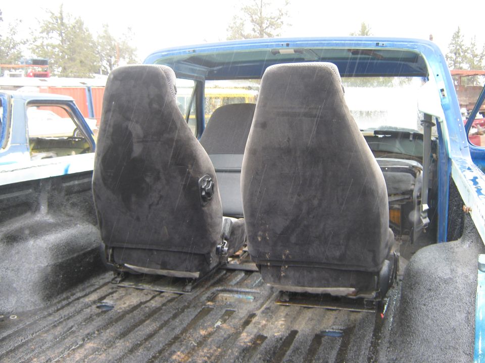 Interior view of a blue pickup truck bed showing two bucket seats and another vehicle in the background