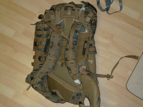 1992 Ford Mustang - A military backpack with MOLLE webbing and adjustable straps is shown from the rear on a wood-grain floor.