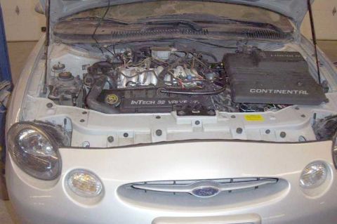 1997 Ford Taurus - The engine bay of a 1997 Ford Taurus is visible with the hood raised, revealing the V6 engine and associated parts.