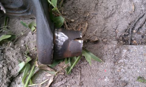 1990 Ford Bronco - A close-up view of a metal automotive part resting on the ground amidst dirt and vegetation.
