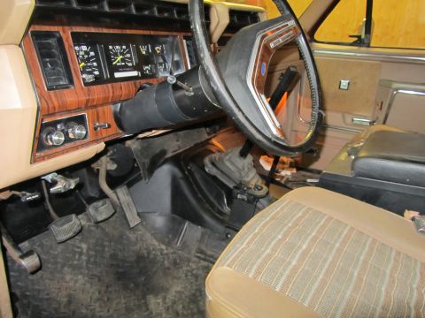 1984 Ford Bronco - The interior of an older vehicle, a wood-grain dashboard and patterned seats.