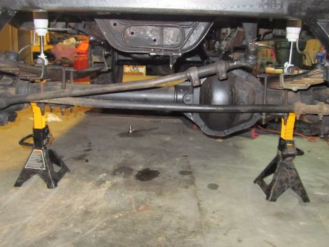 1984 Ford Bronco - The underside of a vehicle is supported by jack stands, revealing its mechanical components.