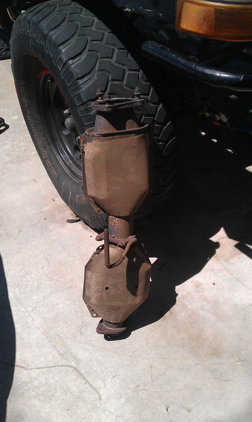 rusted exhaust pipe hanging from a vehicle's undercarriage near a tire