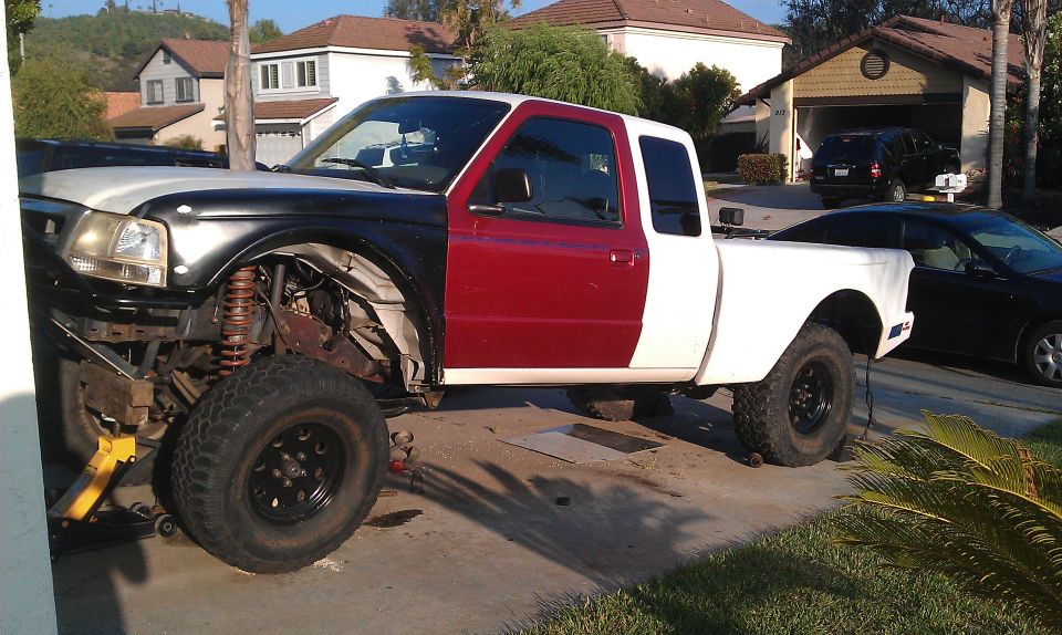 Truck with black front fender, red door, and white bed; front end disassembled