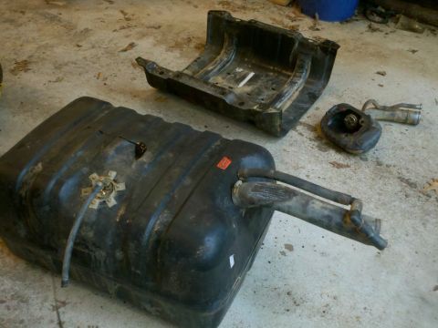 1979 Ford Bronco - A disassembled fuel tank and skid plate lie on a concrete surface.