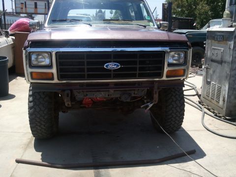 1982 Ford Bronco - Front view of a brown Ford Bronco with large tires and a missing bumper, parked outdoors.