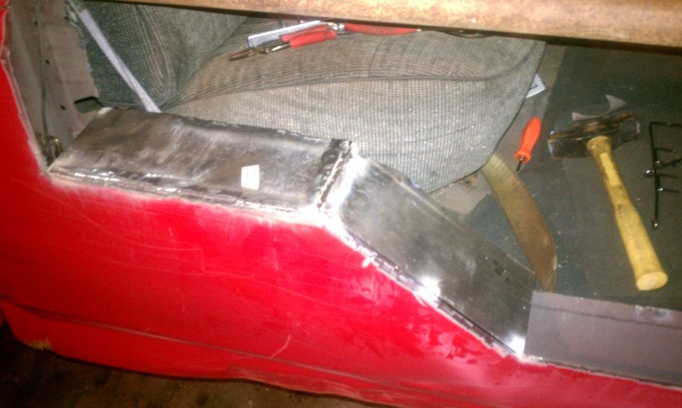 Red vehicle door interior with metal patch and welding marks. Tools are visible