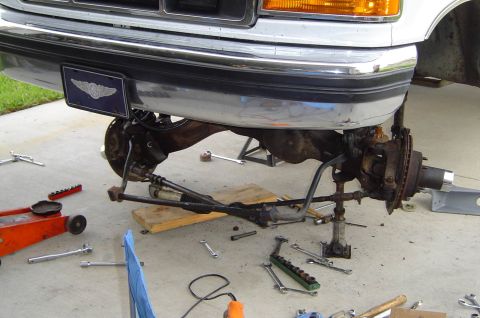 1993 Ford Bronco - Front suspension of a 1993 Ford Bronco undergoing maintenance, with tools scattered around.