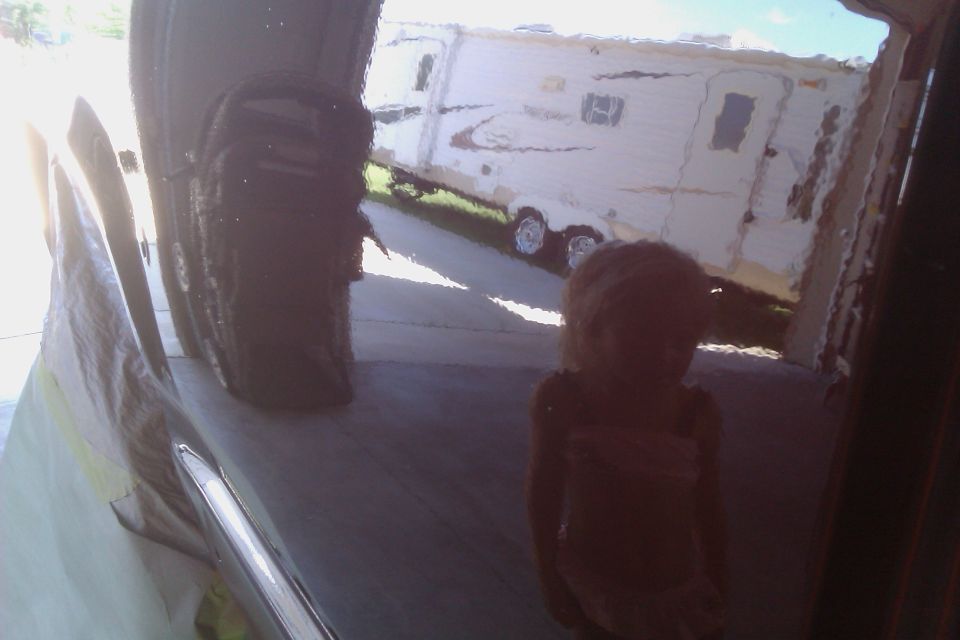 Reflection of a child and a white travel trailer on a dark, reflective surface