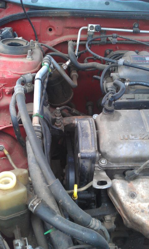 1991 Ford Festiva - Close-up of a car's engine bay, hoses, belts, and the Mazda logo on the valve cover.